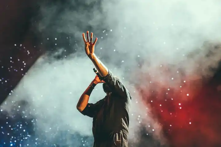 Chanteur sur scène levant la main, entouré de lumière et de fumée, lors d'un concert live