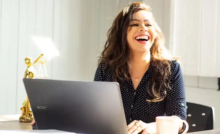 Femme joyeuse travaillant sur un ordinateur portable, tasse de café à la main