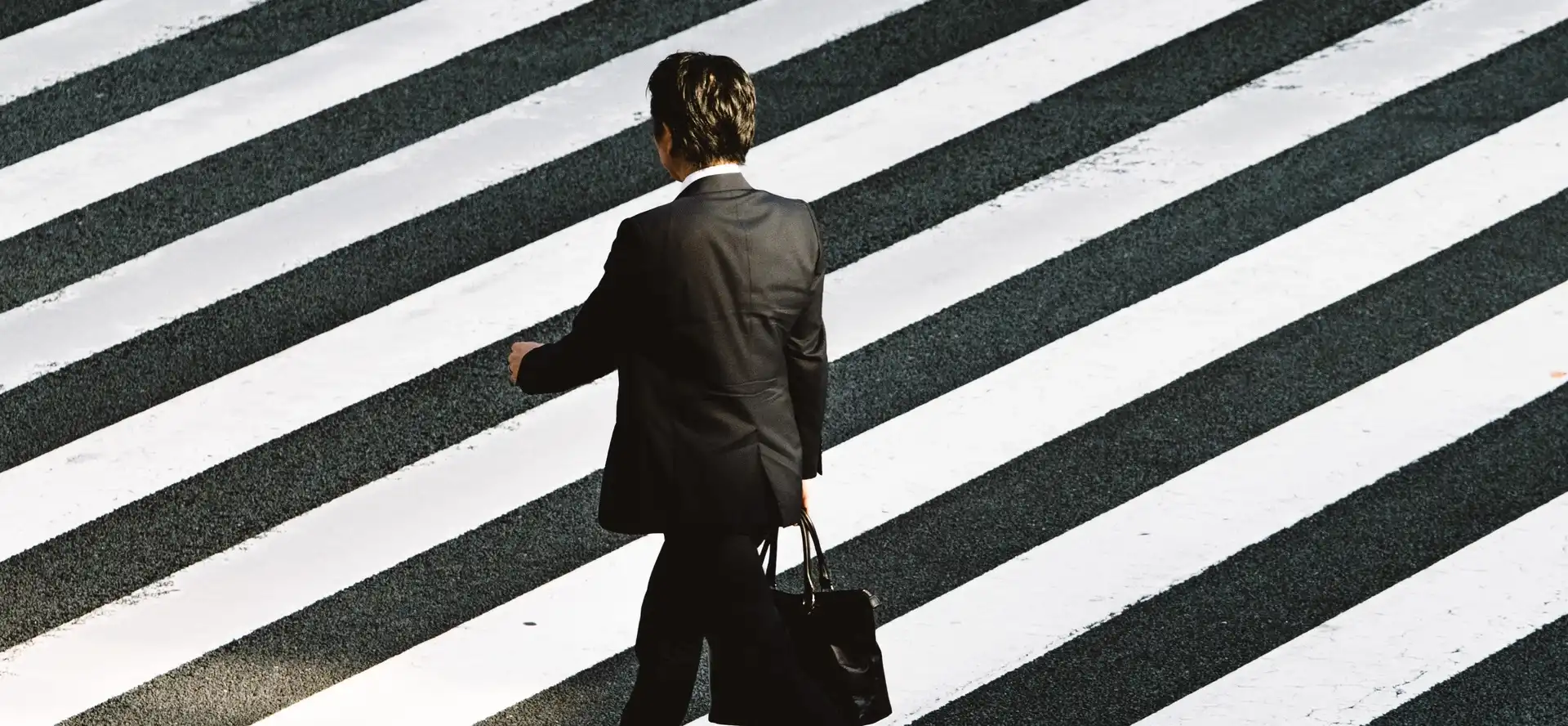 Homme en costume avec une mallette traversant un passage piéton à rayures noires et blanches